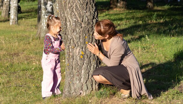 Donna di mezza età che gioca con la bambina che si nasconde dietro l'albero nella foresta