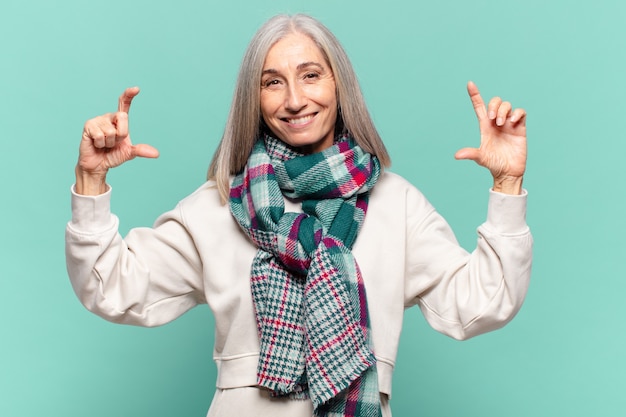 Donna di mezza età che incornicia o delinea il proprio sorriso con entrambe le mani, guardando positivo e felice, concetto di benessere