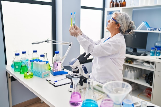 Donna di mezza età che indossa l'uniforme da scienziato alla ricerca di provette in laboratorio