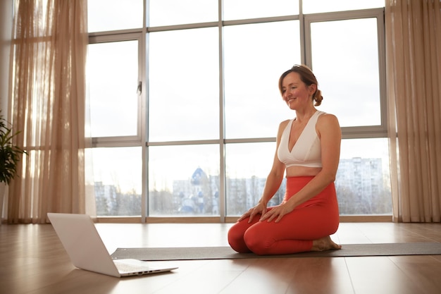 Donna di mezza età che insegna lezioni di yoga online, usando il suo laptop