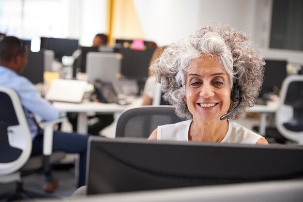 Donna di mezza età che lavora al computer con l'auricolare in ufficio