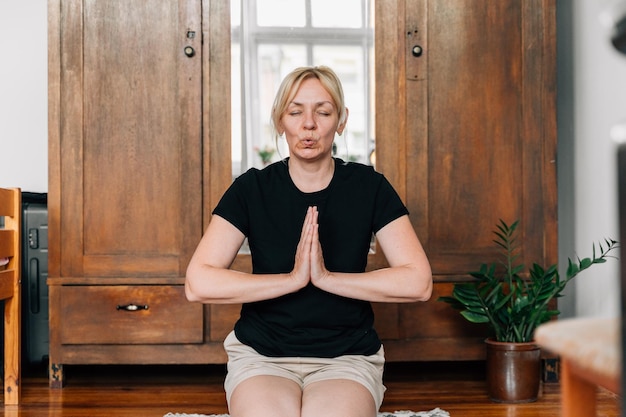 Donna di mezza età che media e fa yoga a casa Esercizio di respirazione per la salute mentale