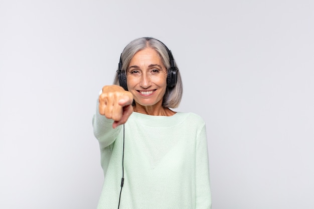 donna di mezza età che punta con un sorriso soddisfatto, fiducioso, amichevole, scegliendo te. concetto di musica