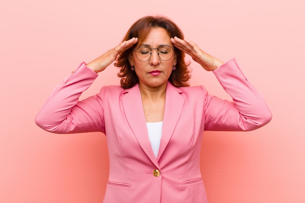 Donna di mezza età che sembra concentrata, riflessiva e ispirata, brainstorming e immaginazione con le mani sulla fronte sulla parete rosa