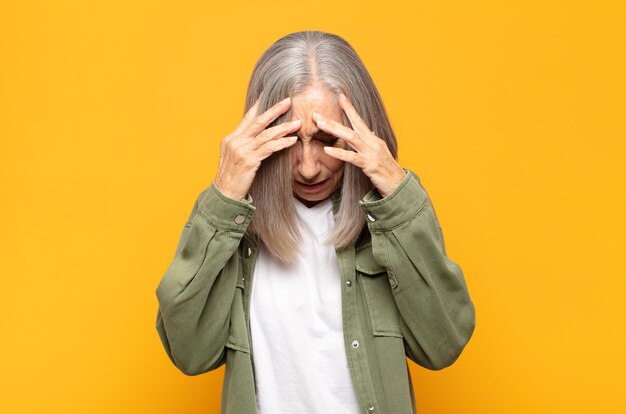 Donna di mezza età che sembra stressata e frustrata, lavora sotto pressione con un mal di testa e tormentata dai problemi