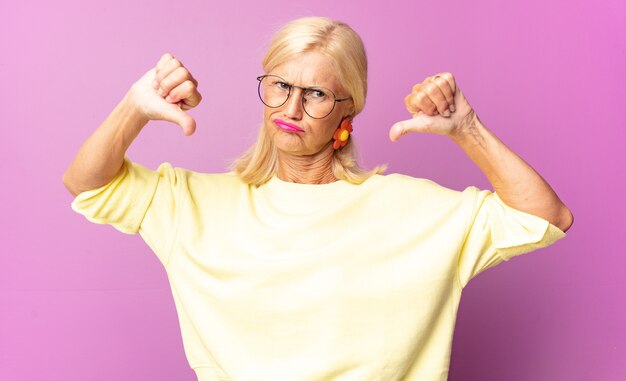 Donna di mezza età che sembra triste, delusa o arrabbiata, che mostra il pollice verso il basso in disaccordo, sentendosi frustrata