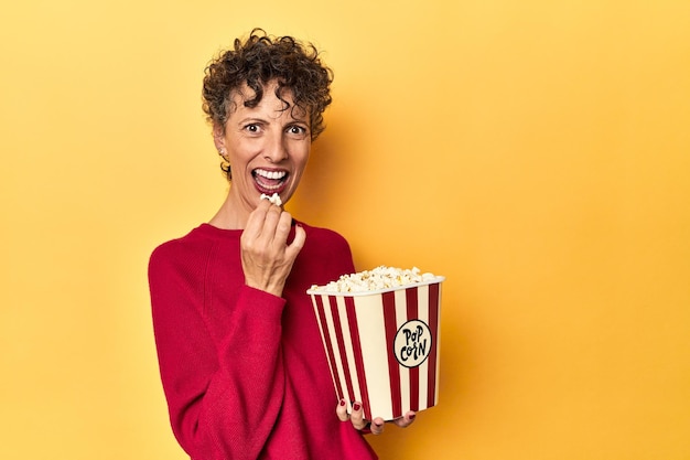 Donna di mezza età che si gode i popcorn per un film su uno sfondo giallo da studio