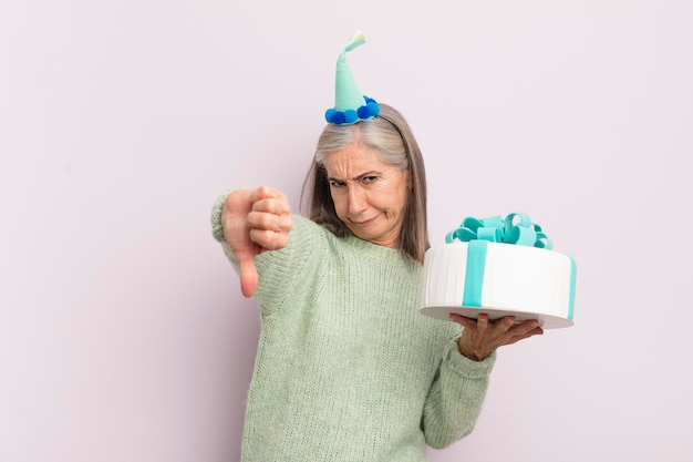 Donna di mezza età che si sente crossshowing pollice verso il concetto di torta di compleanno