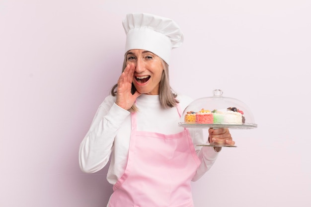 Donna di mezza età che si sente felice un grande grido con le mani accanto al concetto di fornaio e torte della bocca