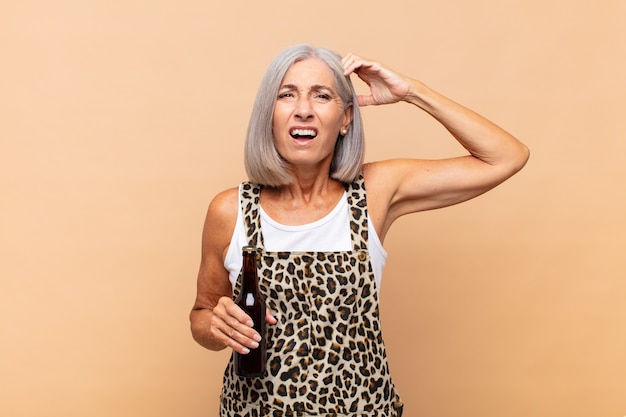 Donna di mezza età che si sente perplessa e confusa, grattandosi la testa e guardando di lato con una birra