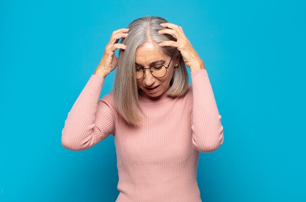 Donna di mezza età che si sente stressata e frustrata, alza le mani alla testa, si sente stanca, infelice e con emicrania