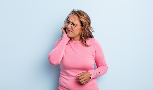 Donna di mezza età che si sente stressata, frustrata e stanca, strofinando il collo doloroso, con uno sguardo preoccupato e turbato