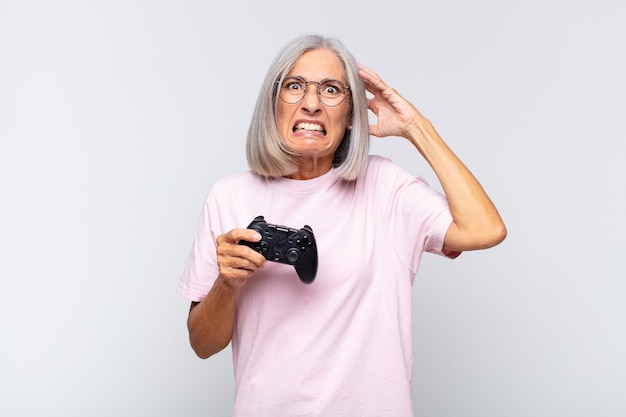 Donna di mezza età che si sente stressata, preoccupata, ansiosa o spaventata, con le mani sulla testa, in preda al panico per errore. giocando il concetto di console