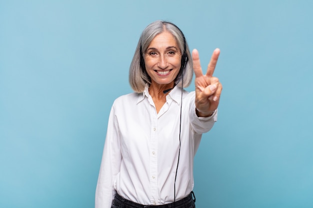 Donna di mezza età che sorride e sembra amichevole, mostrando il numero due o il secondo con la mano in avanti, il conto alla rovescia. concetto di telemarketer