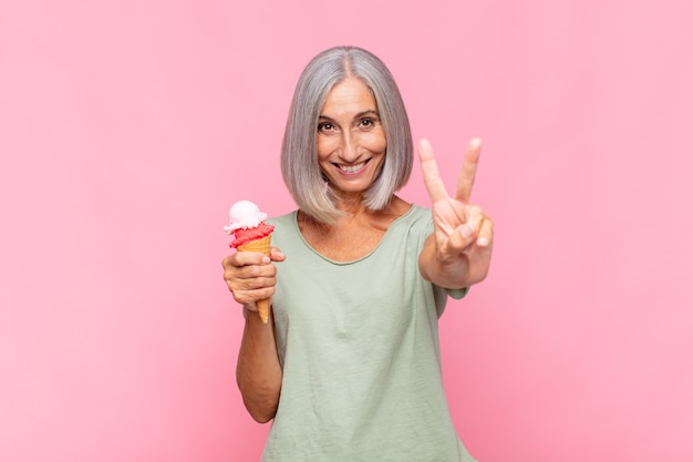 Donna di mezza età che sorride e sembra felice, spensierata e positiva, gesticolando vittoria o pace con una mano con un gelato