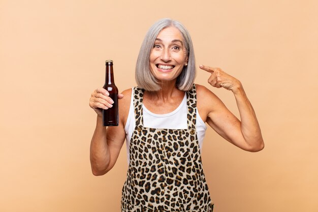 Donna di mezza età che sorride fiduciosamente indicando il proprio ampio sorriso, atteggiamento positivo, rilassato, soddisfatto con una birra