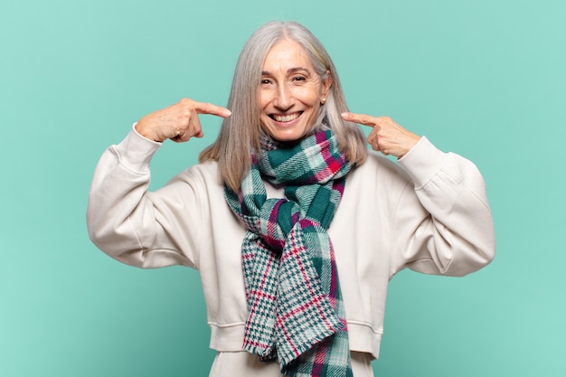 Donna di mezza età che sorride fiduciosamente indicando il proprio ampio sorriso, atteggiamento positivo, rilassato, soddisfatto