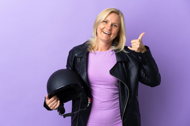 Donna di mezza età che tiene un casco del motociclo isolato sulla parete viola che fa gesto del telefono. Richiamami segno