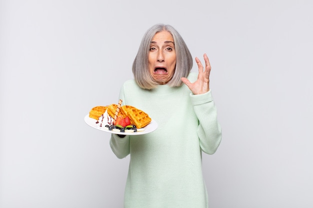 Donna di mezza età che urla con le mani in alto, sentendosi furiosa, frustrata, stressata e sconvolta. concetto di colazione