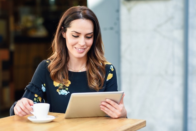 Donna di mezza età che utilizza compressa sulla pausa caffè nella barra urbana del caffè