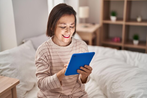 Donna di mezza età che utilizza il touchpad seduta sul letto in camera da letto