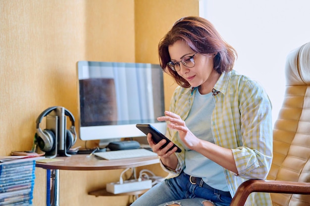 Donna di mezza età che utilizza smartphone seduto in poltrona in ufficio a casa