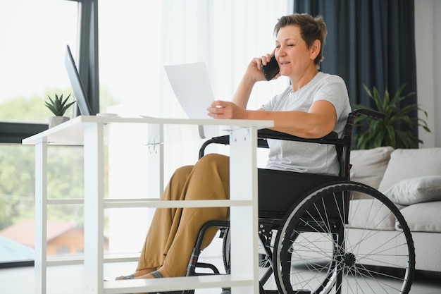 Donna di mezza età che utilizza un laptop seduto su una sedia a rotelle a casa