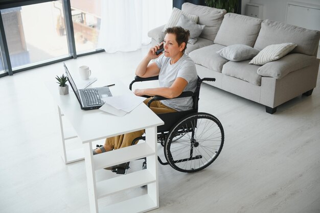 Donna di mezza età che utilizza un laptop seduto su una sedia a rotelle a casa