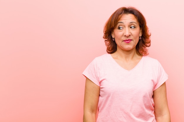 Donna di mezza età chiedendo, pensando pensieri e idee felici, sognare ad occhi aperti, cercando di copiare lo spazio sul lato contro il muro rosa