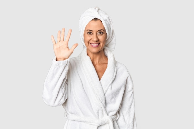Donna di mezza età con asciugamano dopo la doccia in studio sorridente allegro che mostra il numero cinque con le dita