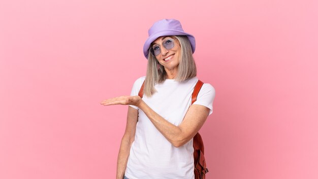 Donna di mezza età con capelli bianchi che sorride allegramente, si sente felice e mostra un concetto. concetto di estate