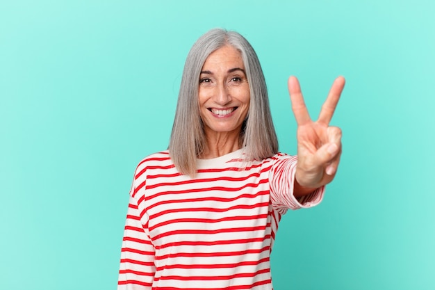 Donna di mezza età con capelli bianchi che sorride e sembra felice, gesticolando vittoria o pace