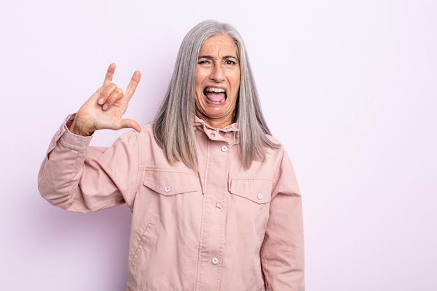 Donna di mezza età con capelli grigi che si sente felice, divertente, sicura di sé, positiva e ribelle, facendo segno rock o heavy metal con la mano