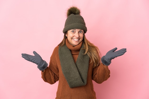 Donna di mezza età con cappello invernale isolato sulla parete rosa con espressione facciale scioccata