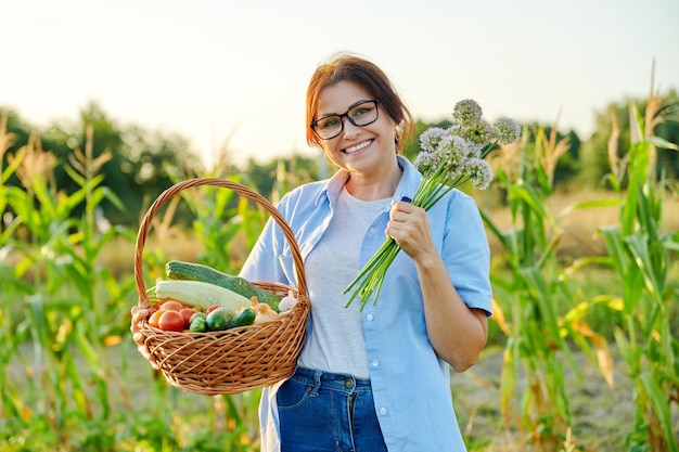 Donna di mezza età con cesto di verdure biologiche fresche nella fattoria del giardino
