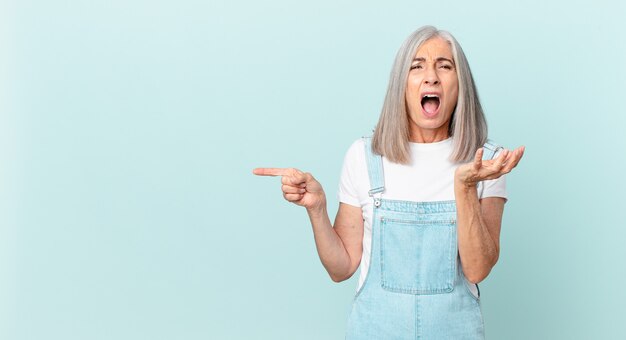 Donna di mezza età con i capelli bianchi che sembra disperata, frustrata e stressata e indica il lato