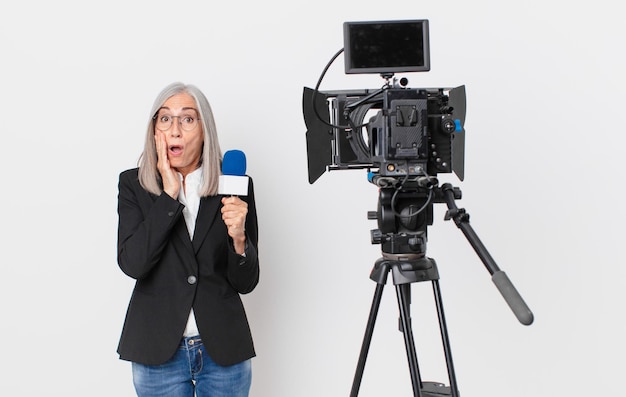 Donna di mezza età con i capelli bianchi che si sente scioccata e spaventata e tiene in mano un microfono. concetto di presentatore televisivo