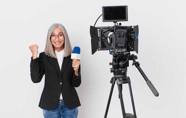 Donna di mezza età con i capelli bianchi che si sente scioccata, ride e celebra il successo e tiene in mano un microfono. concetto di presentatore televisivo