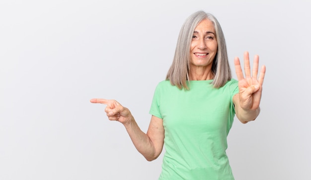 Donna di mezza età con i capelli bianchi che sorride e sembra amichevole, mostra il numero quattro e indica il lato