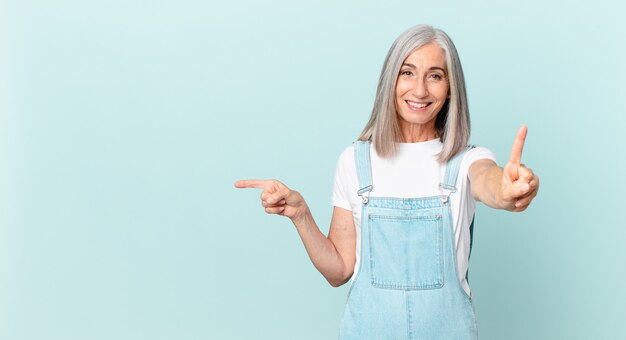 Donna di mezza età con i capelli bianchi che sorride e sembra amichevole, mostra il numero uno e indica il lato