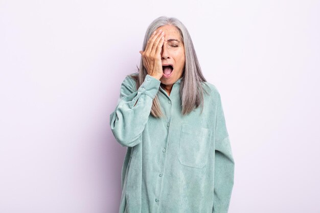 Donna di mezza età con i capelli grigi che sembra assonnata, annoiata e sbadigliante, con mal di testa e una mano che copre metà del viso