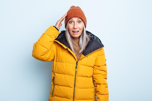 Donna di mezza età con i capelli grigi che sembra felice, stupita e sorpresa. concetto di tempo freddo