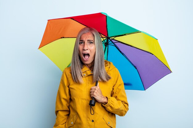 Donna di mezza età con i capelli grigi che sembra molto scioccata o sorpresa. concetto di ombrello e pioggia