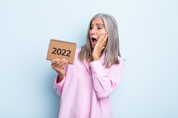 Donna di mezza età con i capelli grigi che si sente felice, eccitata e sorpresa. Concetto di calendario 2022