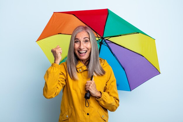 Donna di mezza età con i capelli grigi che si sente scioccata, ride e celebra il successo. concetto di ombrello e pioggia