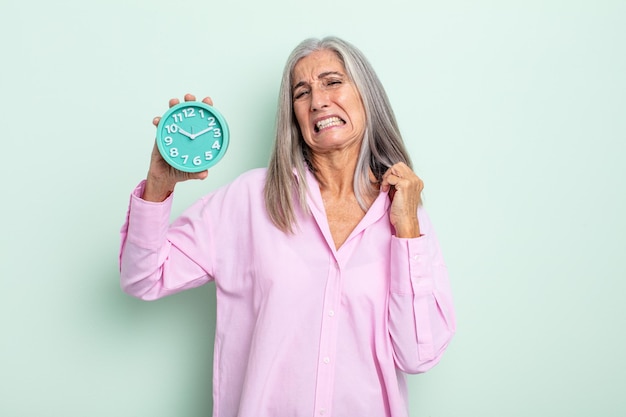 Donna di mezza età con i capelli grigi che si sente stressata, ansiosa, stanca e frustrata. concetto di sveglia