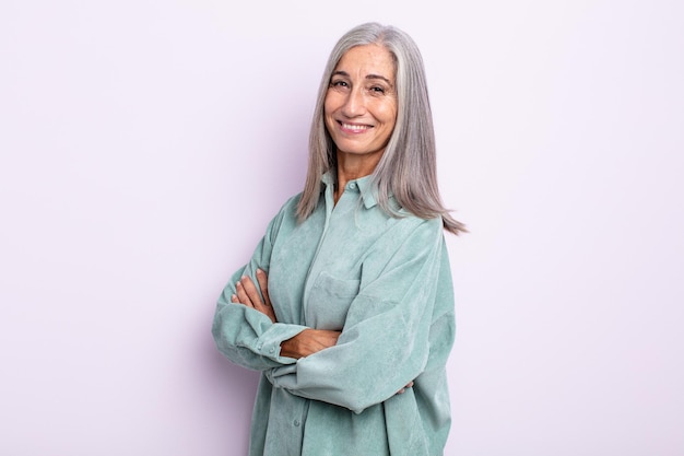 Donna di mezza età con i capelli grigi che sorride alla telecamera con le braccia incrociate e un'espressione felice, sicura e soddisfatta, vista laterale