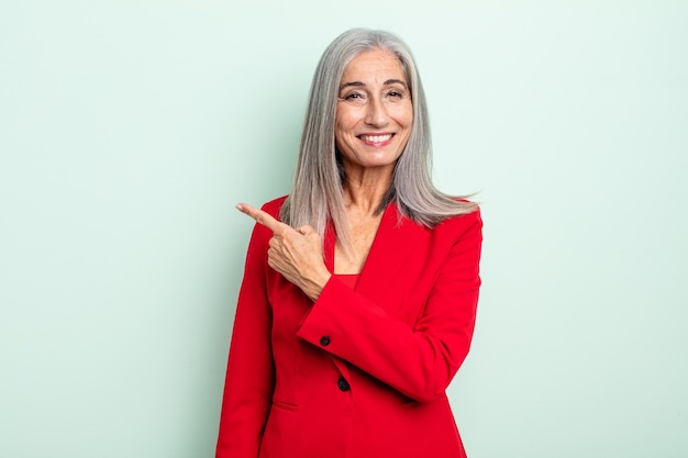 Donna di mezza età con i capelli grigi che sorride allegramente, si sente felice e indica il lato. concetto di donna d'affari senior