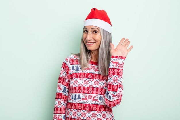 Donna di mezza età con i capelli grigi che sorride felicemente, agitando la mano, dandoti il benvenuto e salutandoti. concetto di natale