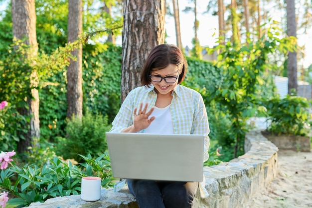 Donna di mezza età con la tazza del computer portatile che riposa lavorando nel cortile